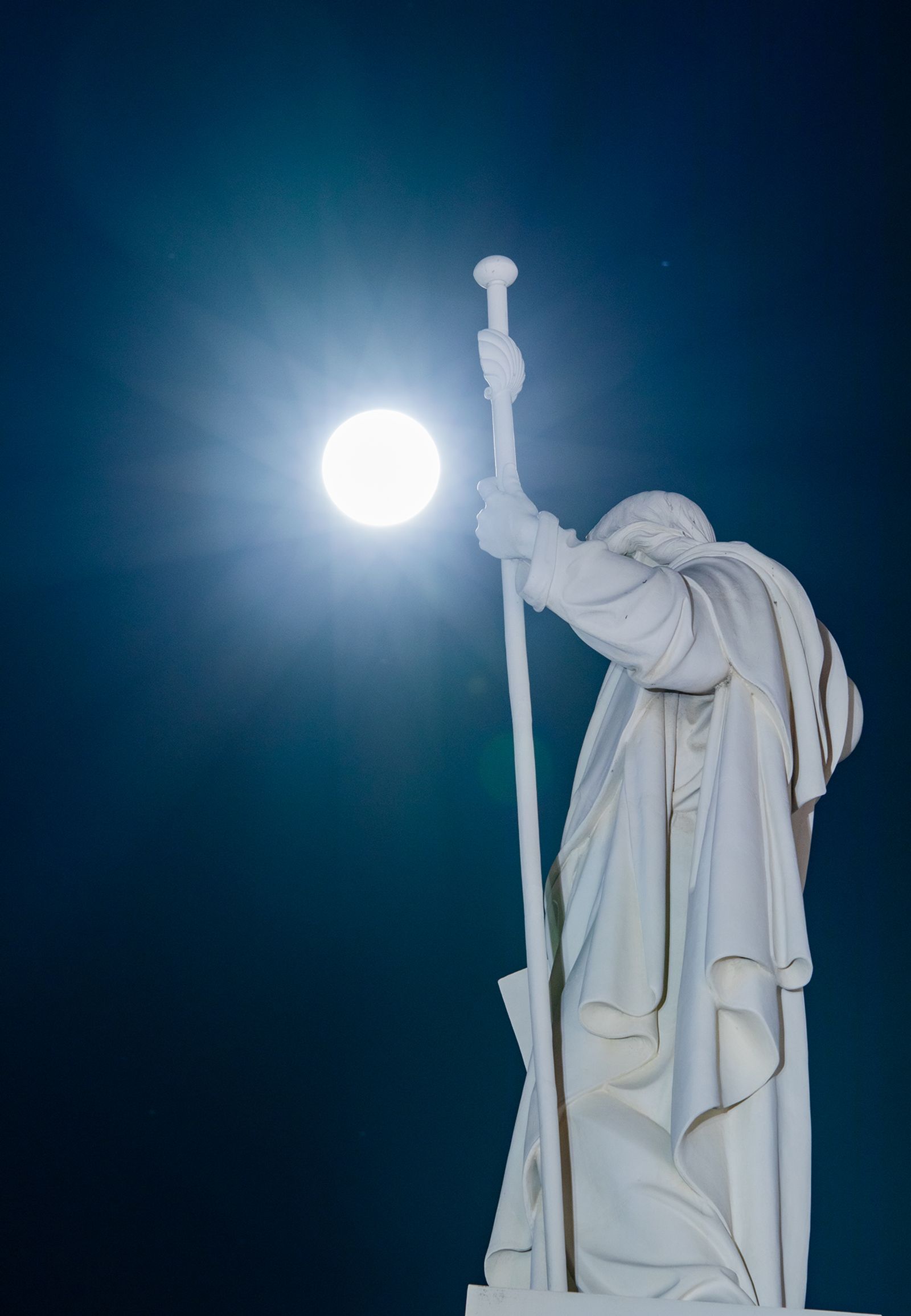Sauvaa kädessä pitävä Helsingin Tuomiokirkon patsas, sekä valkoisena hehkuva kuu sen takana