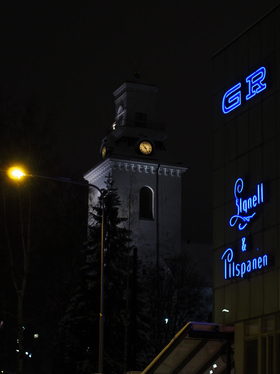 Kuopion kirkko pimeällä, vieressä on läheisen rakennuksen neon-kyltit.